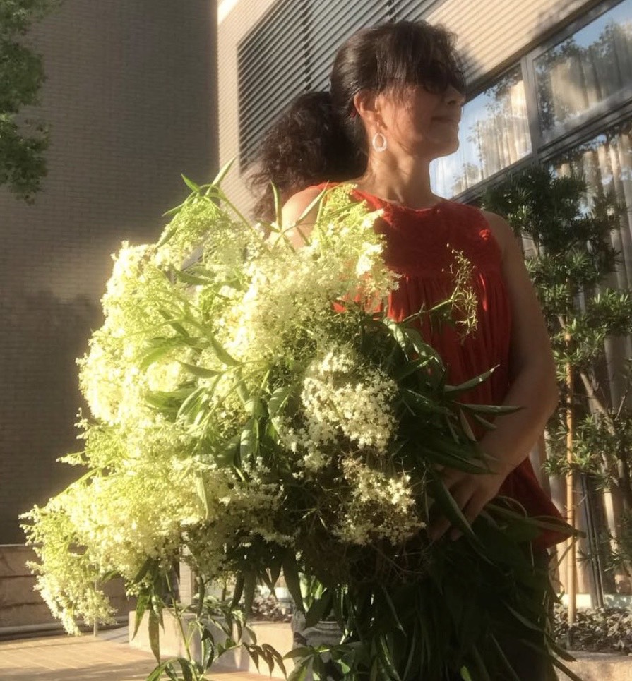 Julia 抱著剛採收的接骨木花束,穿著紅洋裝在夕陽下微笑